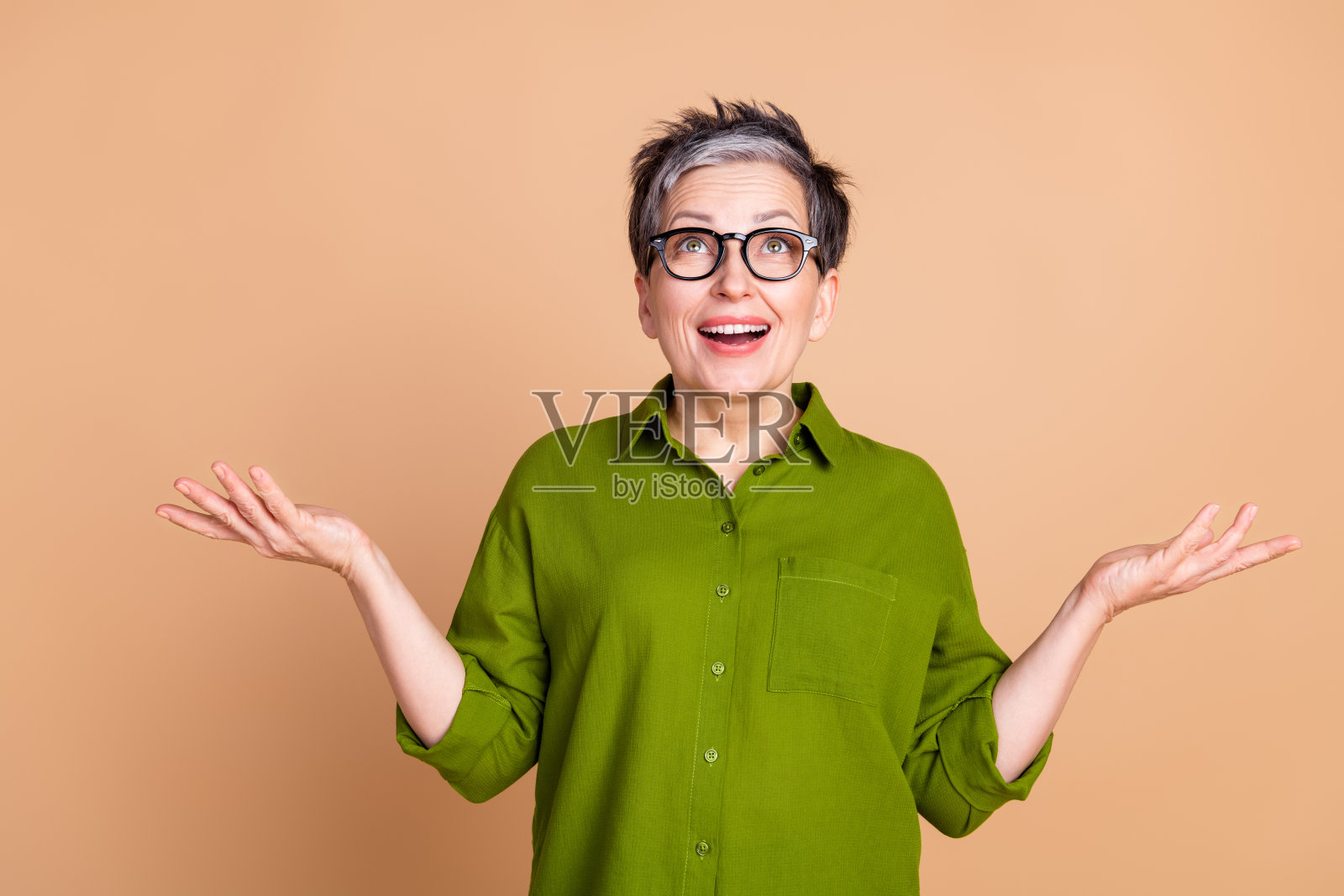 可爱的退休女士的照片肖像仰望空旷的空间，兴奋地穿着时尚的绿色服装，孤立在米色背景上照片摄影图片