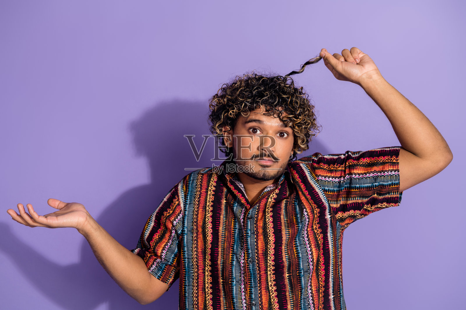 照片上的男人满脸胡须，卷发，穿着印花衬衫，手臂挽着卷发，孤立在紫色的背景上照片摄影图片