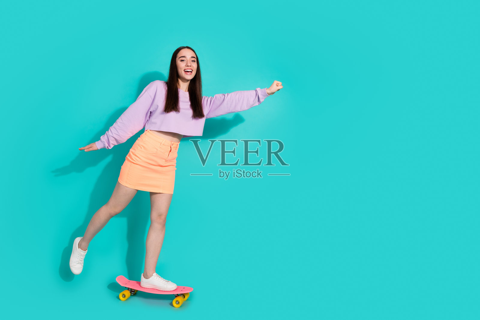 可爱的年轻女士的全身照片骑滑板超人穿着时尚的紫色服装孤立的海蓝宝石色背景照片摄影图片