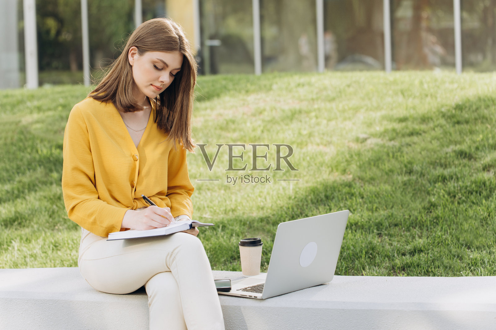 年轻的白人女大学生使用笔记本电脑在线学习，记笔记，观看网络研讨会或虚拟教育远程课程，坐在校园外进行户外学习照片摄影图片