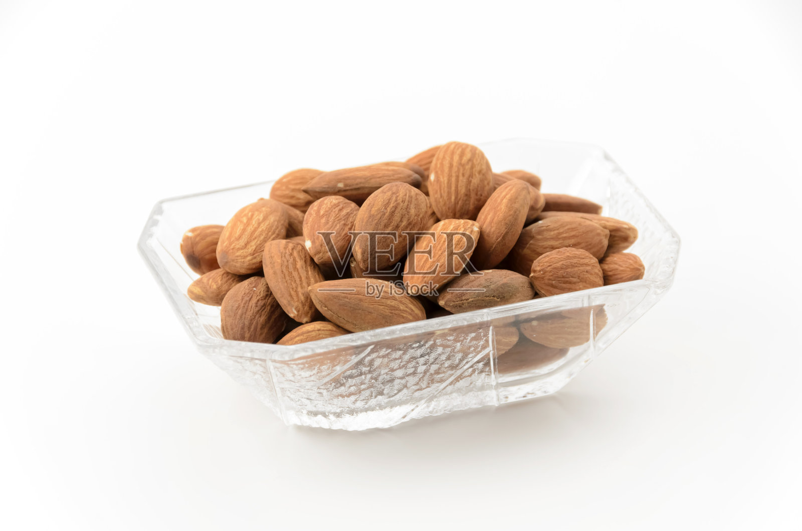 在一个白色背景的小玻璃碗里放上未上釉的杏仁照片摄影图片