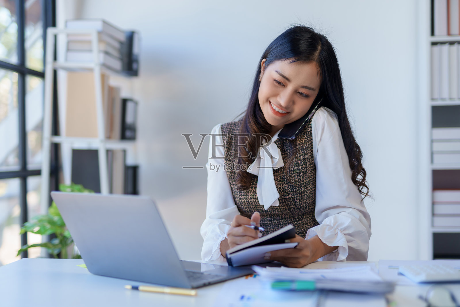 专业的亚洲商务女性坐在办公室里用笔记本电脑工作和打电话。照片摄影图片