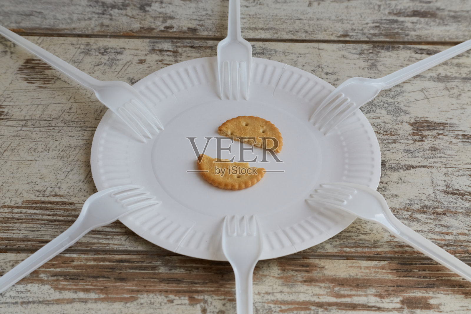 一块饼干在一个一次性盘子里切成两半，盘子周围有六把叉子，木制背景，特写，食品价格上涨，严格的饮食，卡路里限制，微薄的饮食照片摄影图片