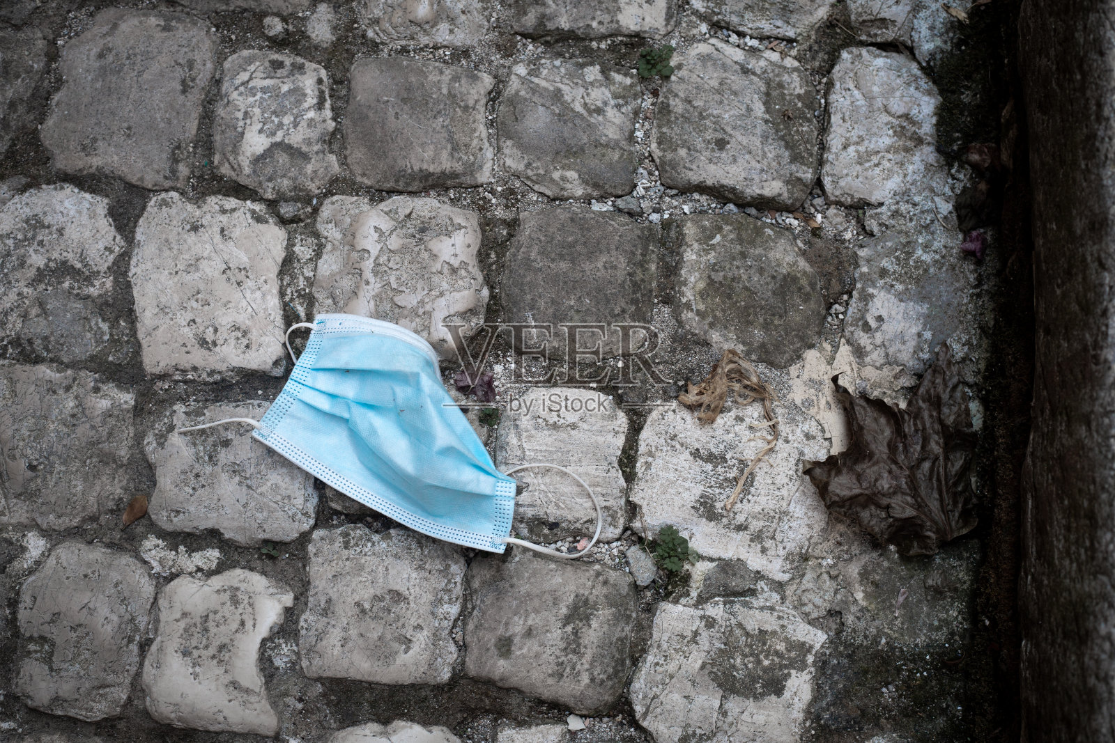 水平的画面。使用过的蓝色医用桅杆FFTP-2在灰色的鹅卵石路面上皱眉。黑白配蓝。对比照片。污染的概念。冠状病毒。生态和循环利用。照片摄影图片