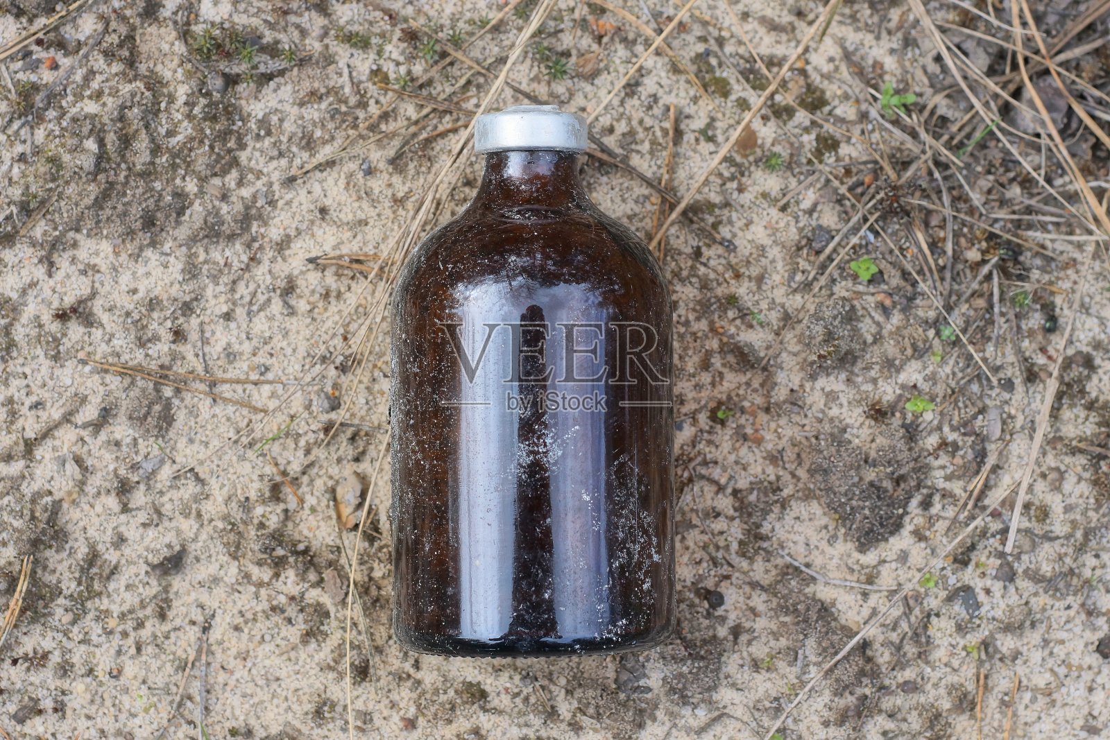 街上灰色的沙滩上躺着一个小小的棕色玻璃瓶，上面有一个标签照片摄影图片