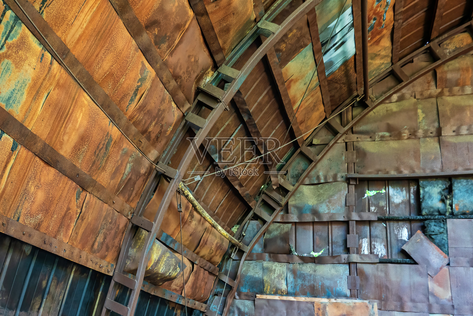 旧半圆形机库内部的一部分。结构上有金属元素，墙壁上有生锈的铁皮。背景。照片摄影图片