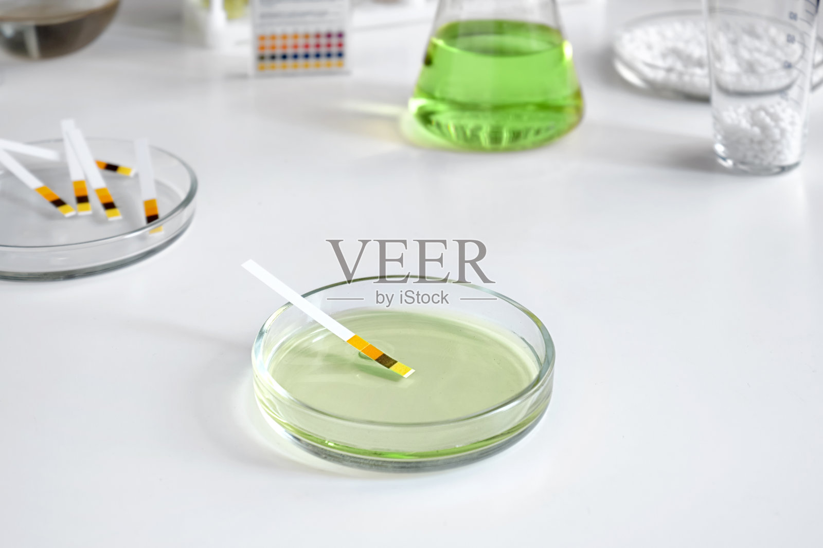 实验室皮氏培养皿的近景，用试纸在化学工具和玻璃器皿的背景下测试碱性酸性溶液。照片摄影图片