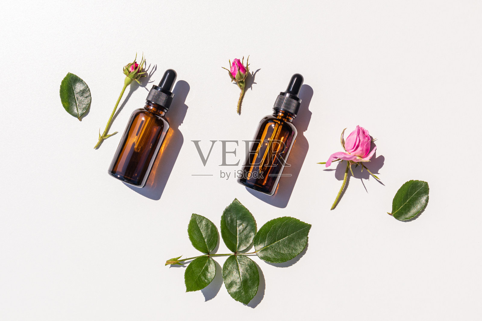 一个天然化妆品在两个瓶子与深色玻璃移液管，玫瑰精油，玫瑰花瓣为基础的精华在玫瑰花蕾。前视图。平躺照片摄影图片