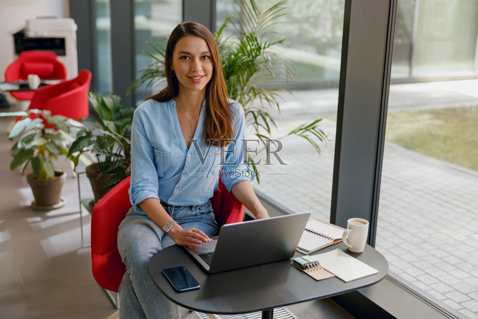 一个自信的女人在一个充满绿色植物的现代办公空间里使用笔记本电脑照片摄影图片