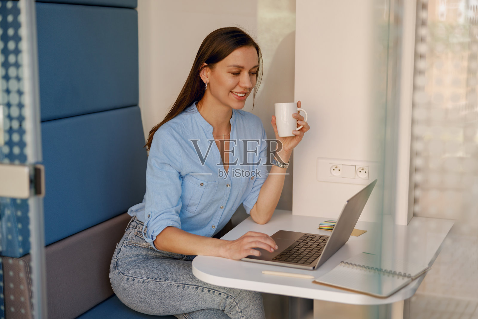 在办公桌前拿着笔记本电脑工作的女人，穿着蓝色衬衫，看起来轻松而高效照片摄影图片