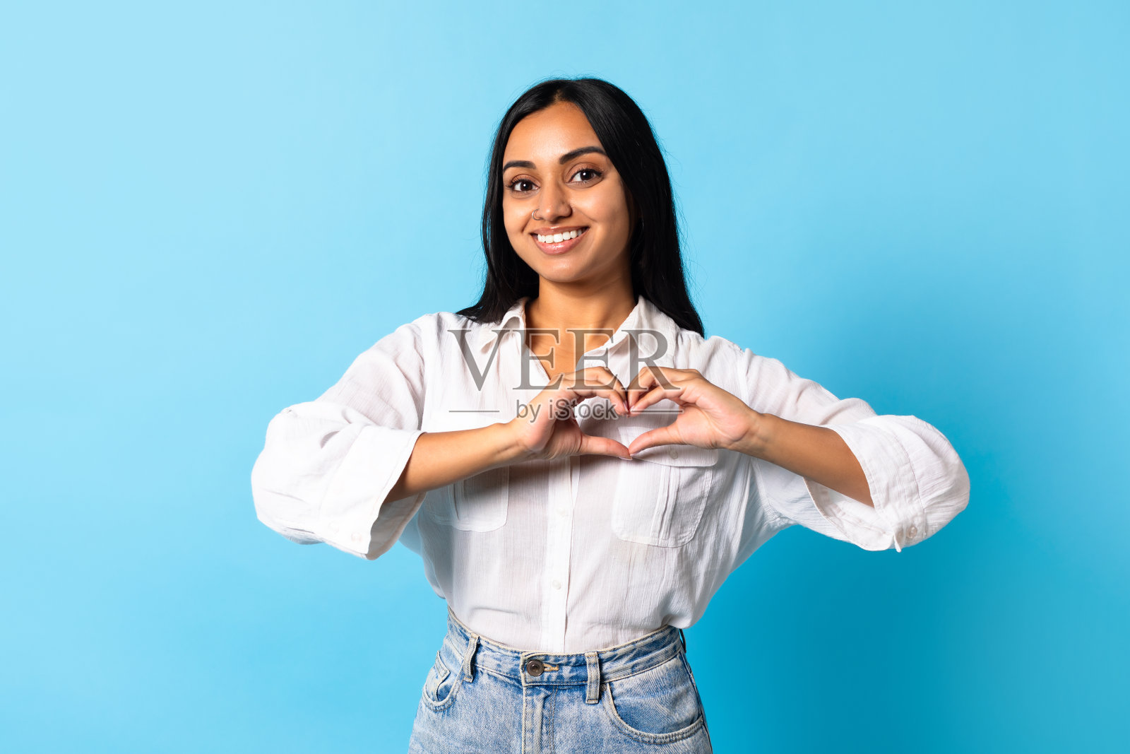 年轻的印度女士用手指做心形手势，蓝色背景照片摄影图片