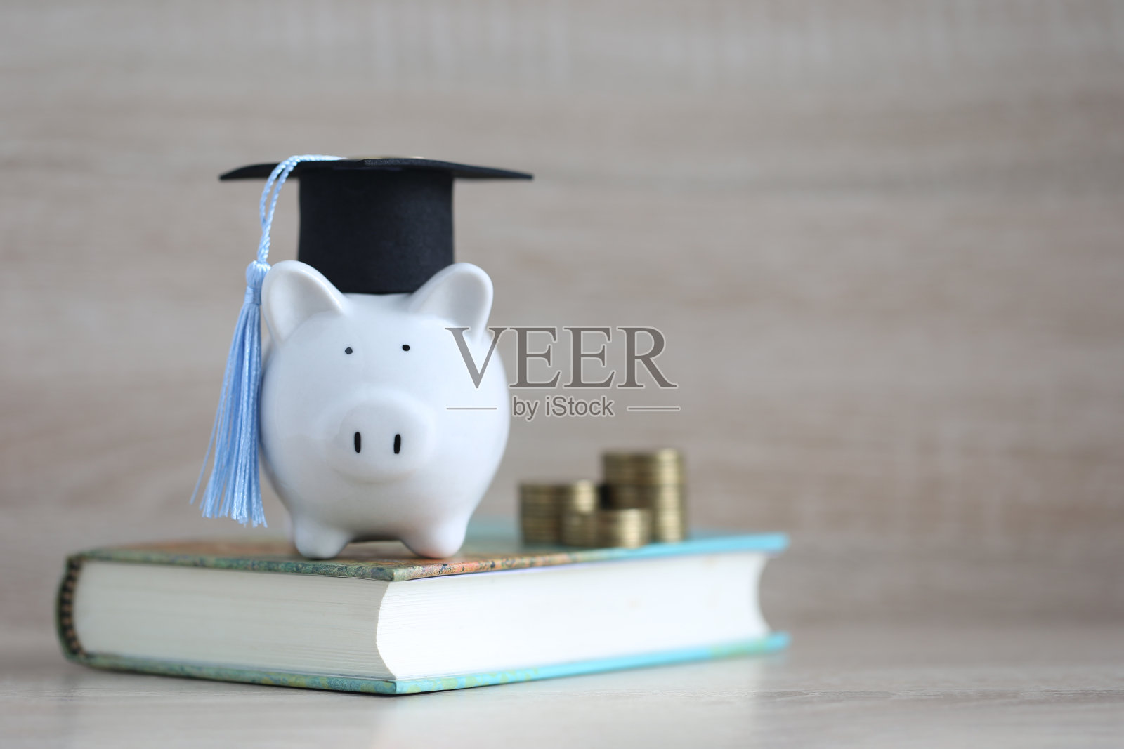 毕业帽上的储蓄罐，木质背景上的一叠硬币，为教育存钱的理念照片摄影图片