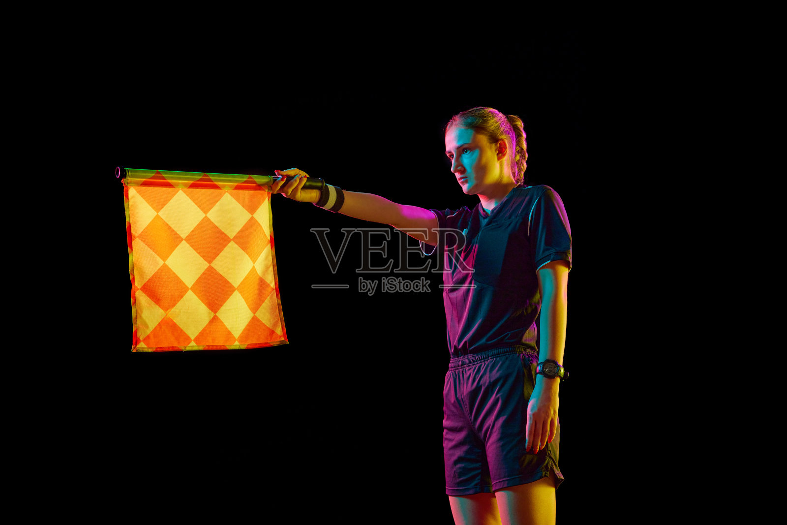 年轻女子，助理裁判，在霓虹灯的黑色工作室背景下，举起代表越位的旗帜照片摄影图片