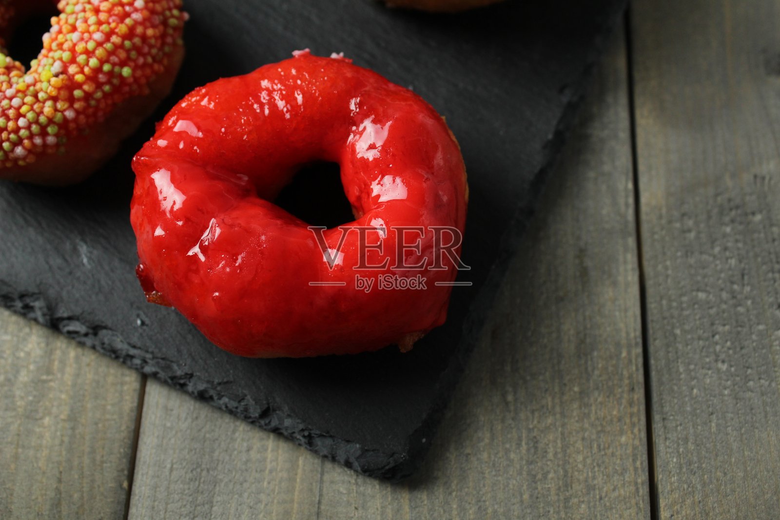 一个在黑色背景上釉上有一个洞的红色甜甜圈特写。不节食的一天是低热量的甜点。国家食品照片摄影图片