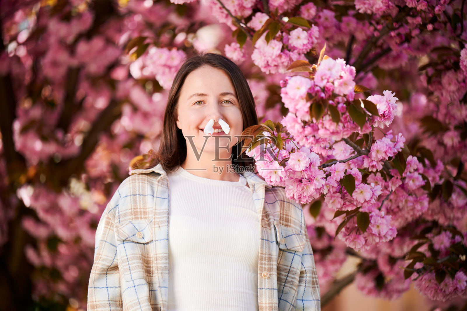 一名妇女在鼻子里塞了纸巾，在春天患上了季节性过敏。照片摄影图片