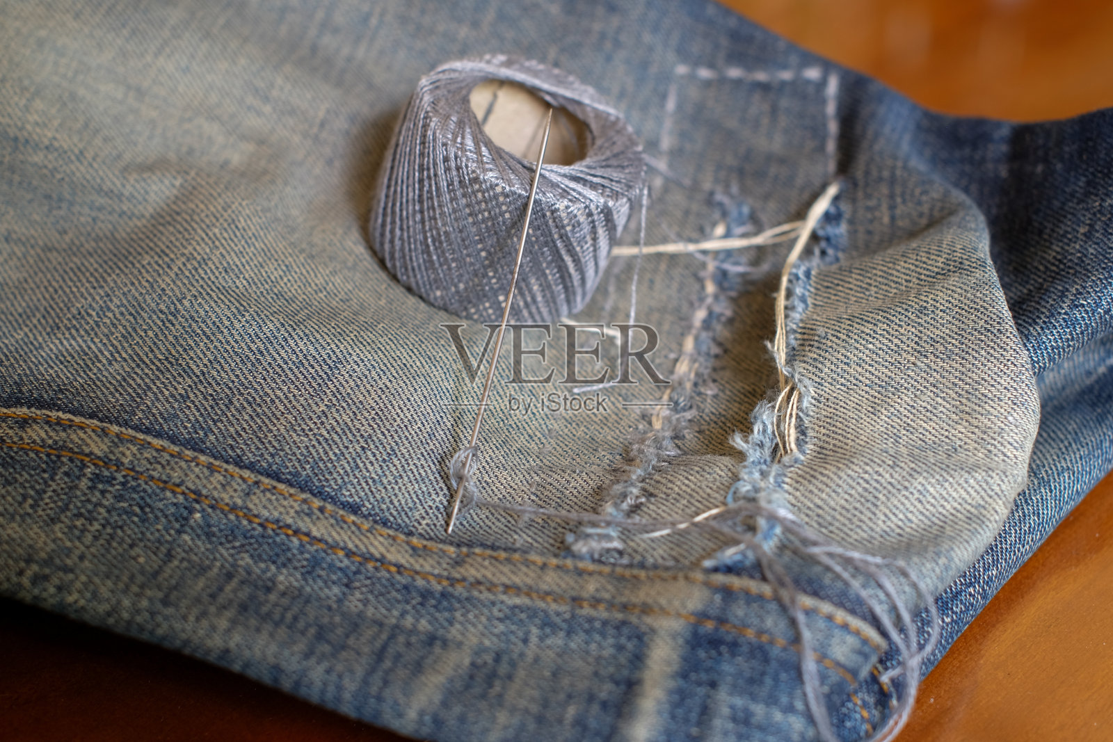 针线在牛仔布上缝了一个洞。针线活女裁缝或裁缝的针线活照片摄影图片