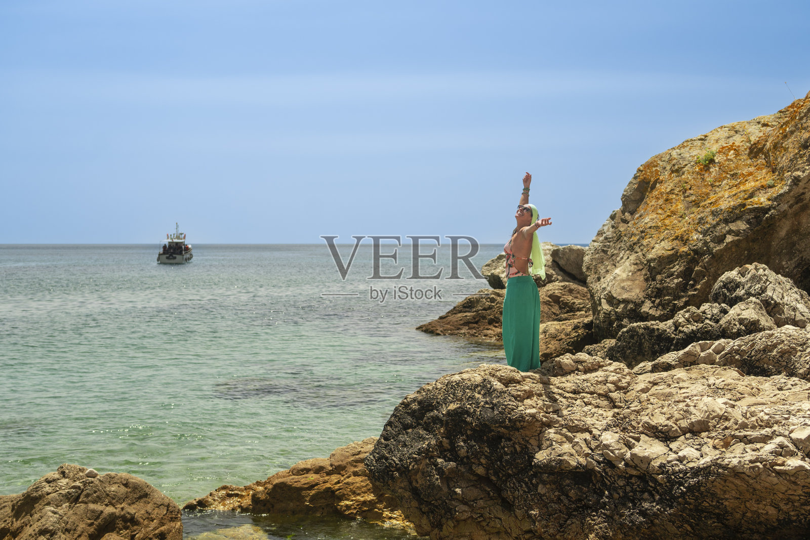 一个女人站在岩石上，张开双臂，面朝大海练习瑜伽照片摄影图片