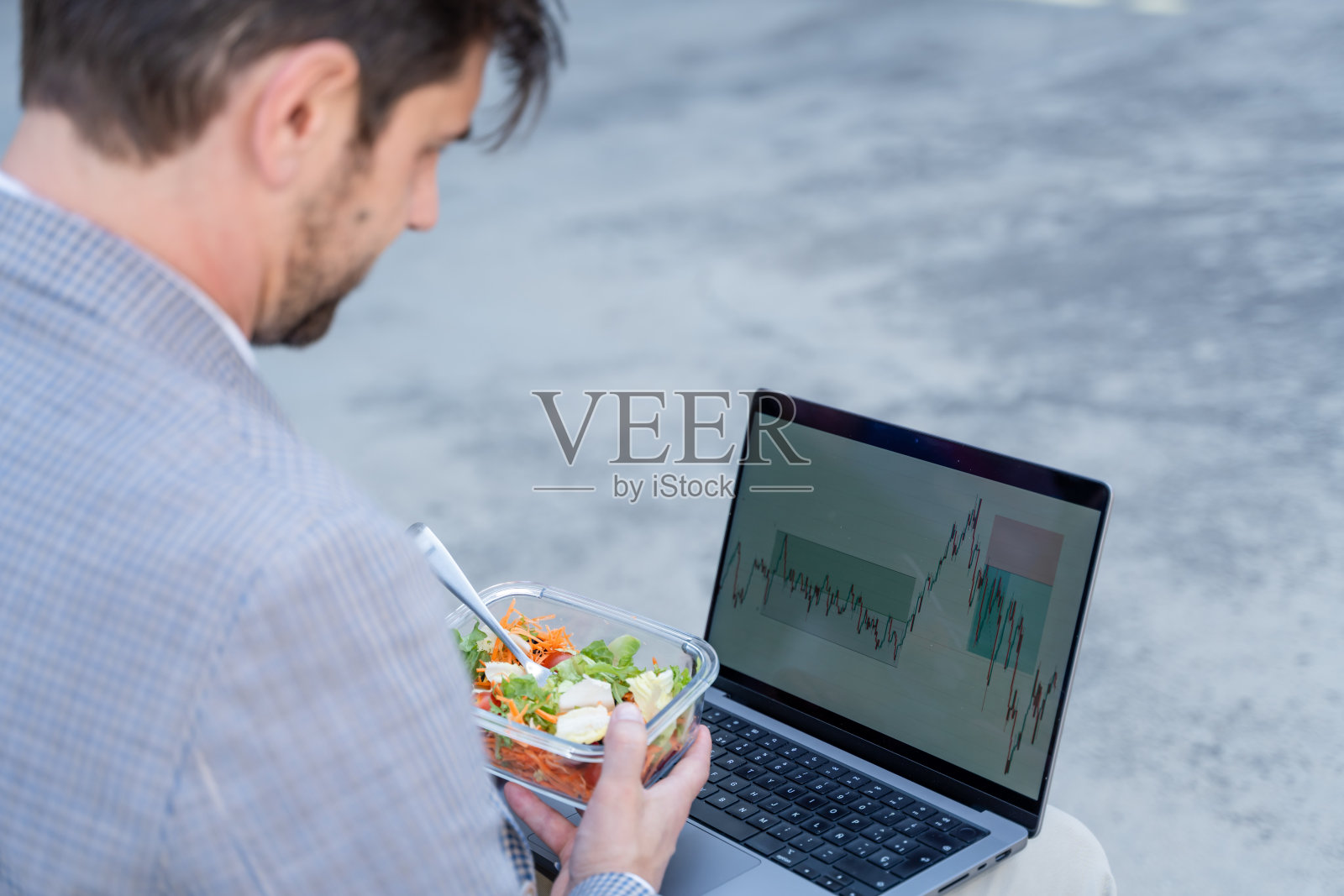 商人一边吃沙拉，一边用笔记本电脑看股市图表照片摄影图片