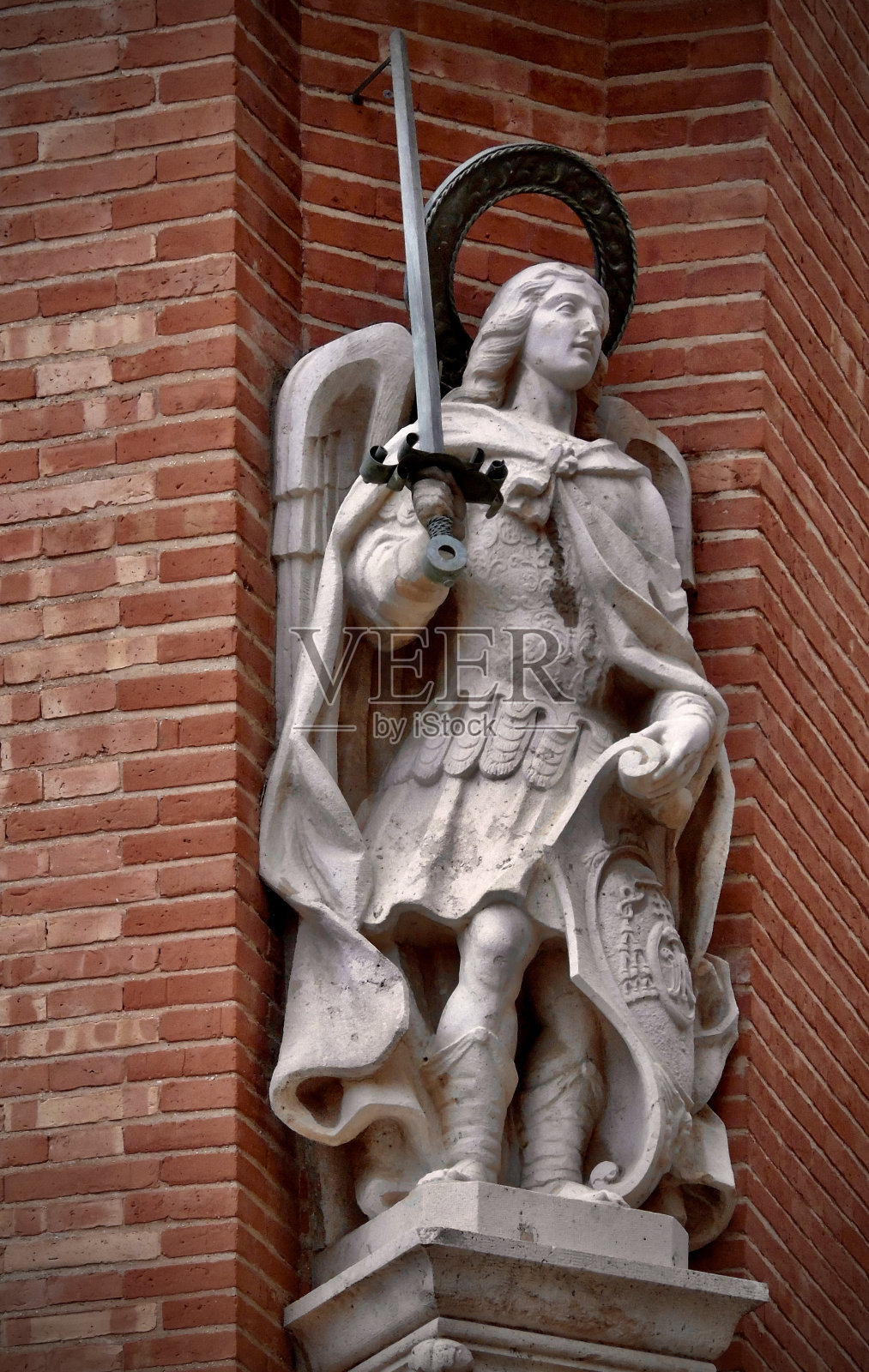 圣米迦勒大天使站在瓦伦蒂亚大教堂砖砌的外墙角落里，手里拿着剑和盾照片摄影图片