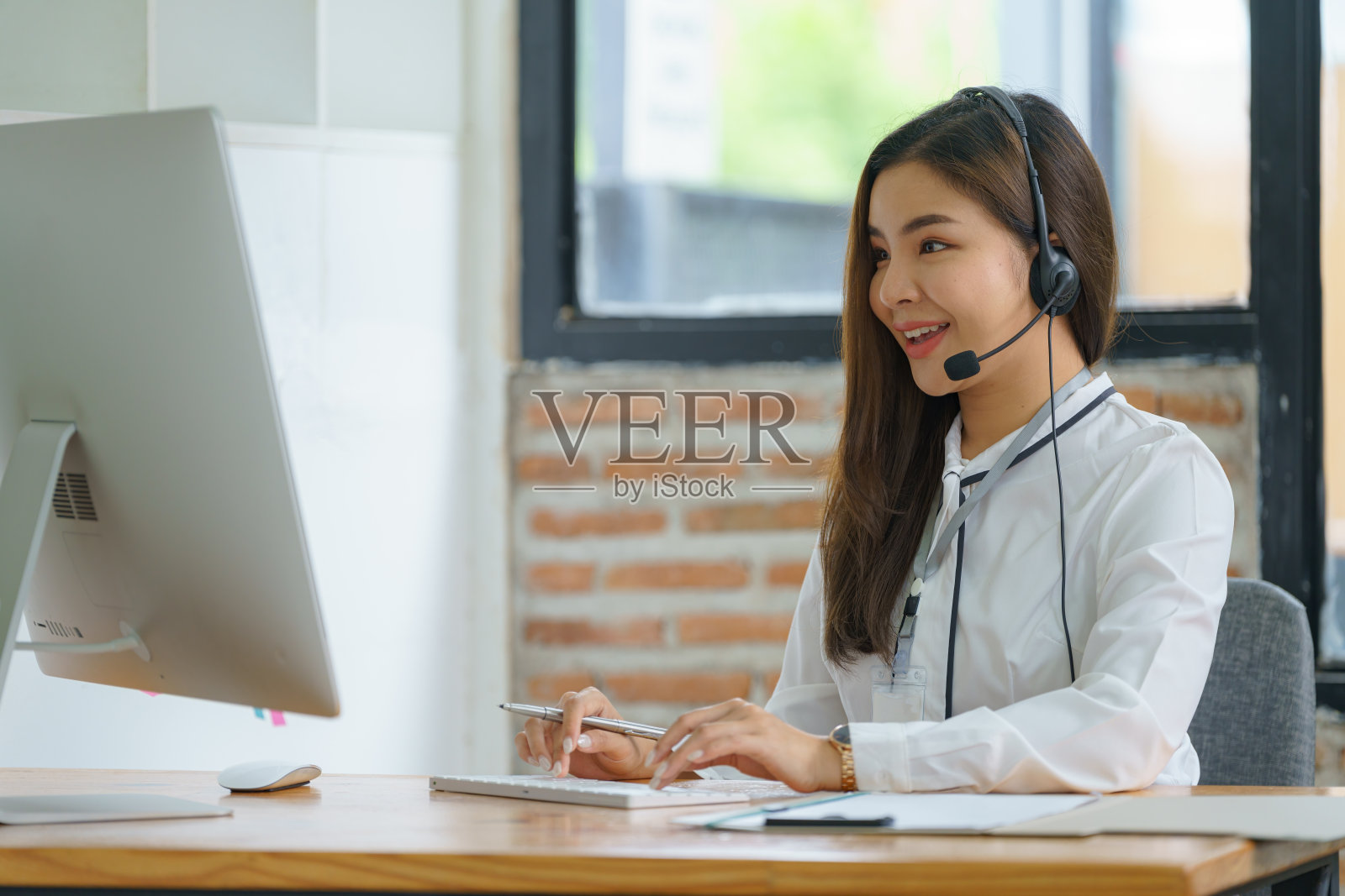 快乐微笑的接线员亚洲女性客户服务代表戴着耳机在呼叫中心的电脑上工作。照片摄影图片