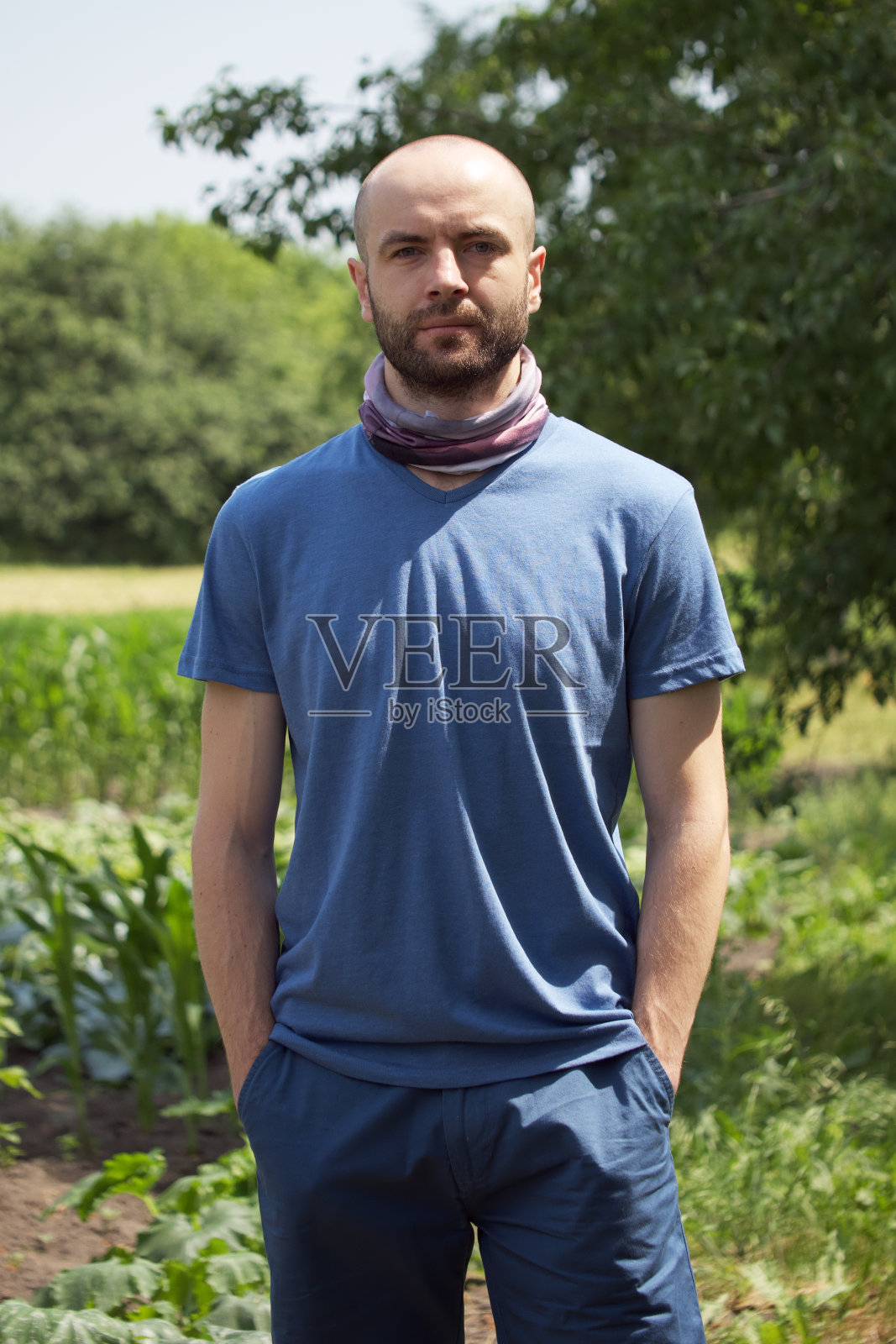 穿蓝色t恤和短裤的白人。一个脸上留着胡茬的秃顶男人把手插在口袋里。看着镜头。照片摄影图片