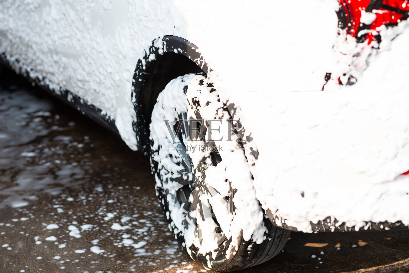 肥皂和泡沫。泡沫从汽车的后轮拱滴到电动汽车的轮胎和轮辋的特写镜头。夏季洗车。使用高压水和洗发水清洗汽车。照片摄影图片