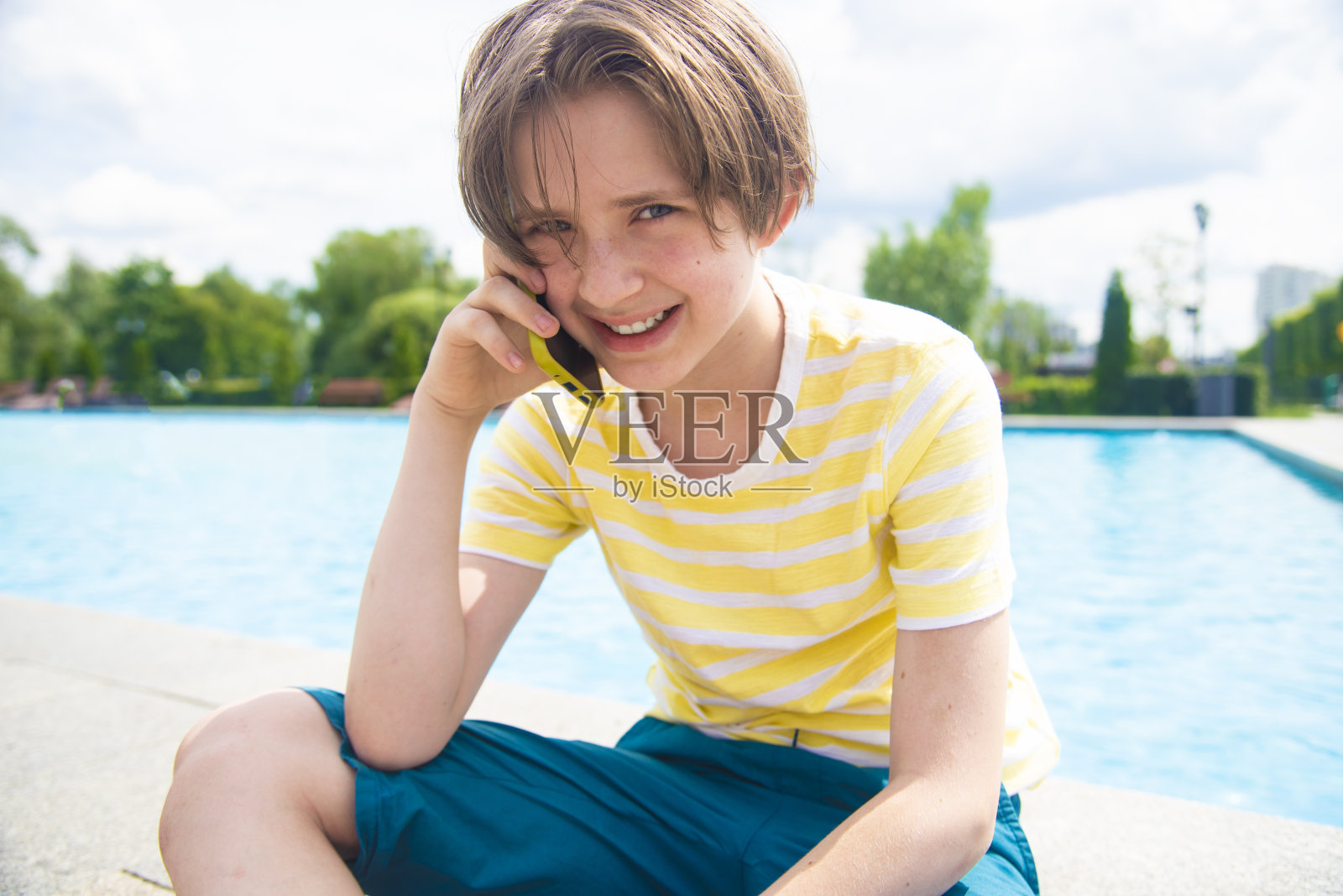 11岁的男孩在假期里坐在泳池前用智能手机交流照片摄影图片