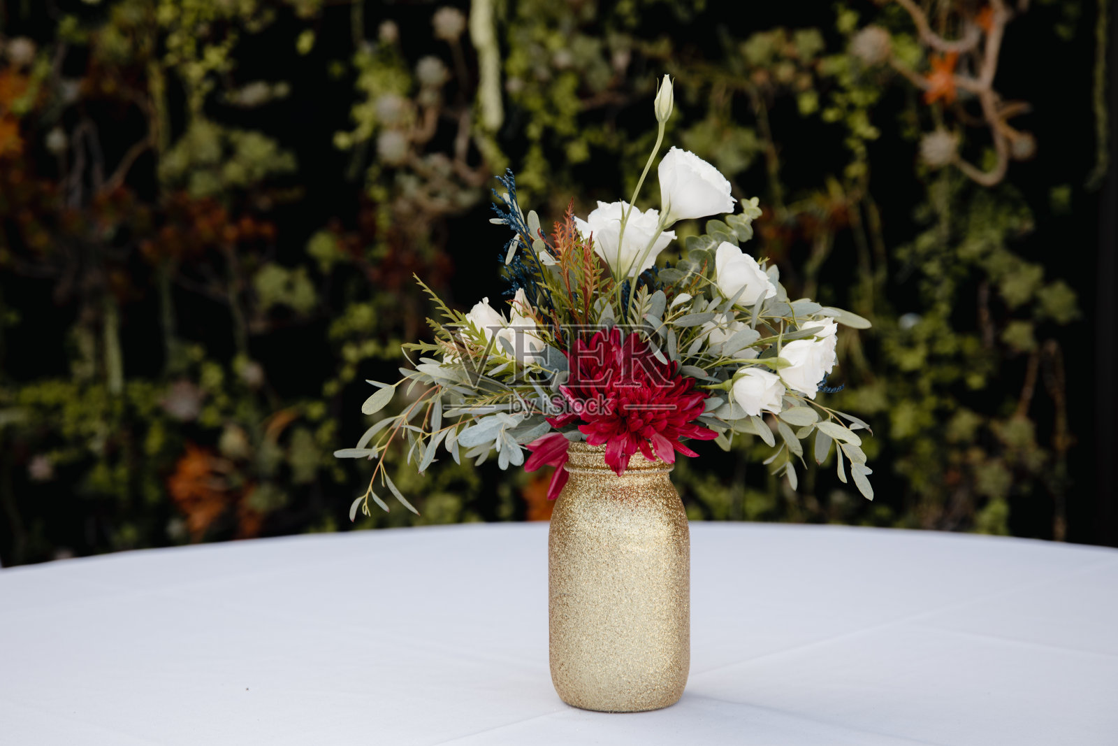 户外婚宴-宾客桌装饰。金色闪光花瓶与酒红色的牡丹，桉树叶花卉安排照片摄影图片