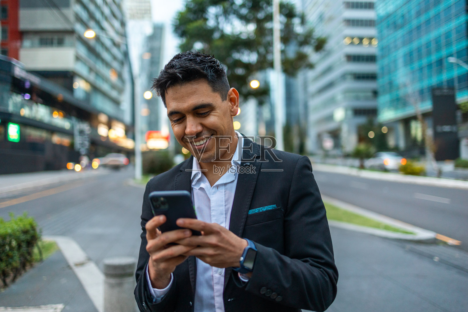 一幅年轻的肖像，微笑着，快乐，成功的墨西哥商人，行政人员走在外面的街道上使用手机。照片摄影图片