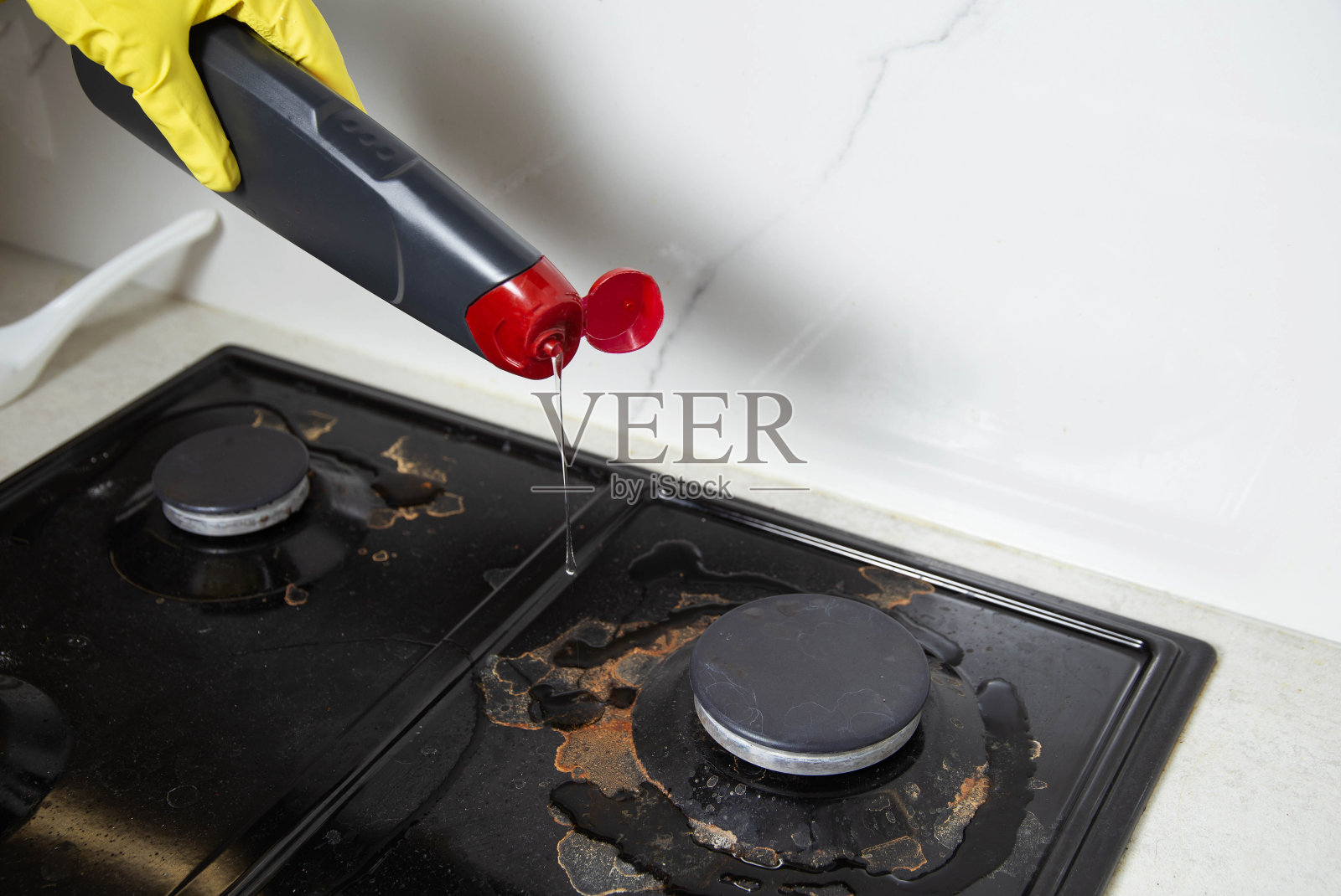 一个戴着黄色手套的女孩的手在厨房的内置煤气炉上清洗污垢和积炭。清洁厨房电器。文本复制空间照片摄影图片