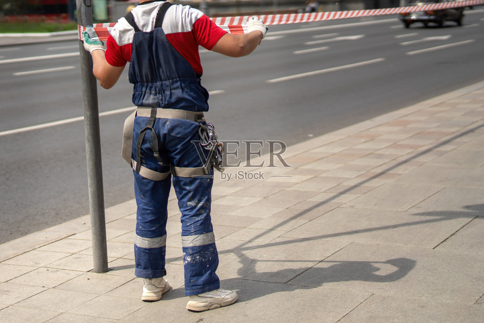 为了行人安全，工业登山运动员在人行道上用红白胶带围起了齿轮围栏，展示了安全防范措施和城市维护的专业性照片摄影图片