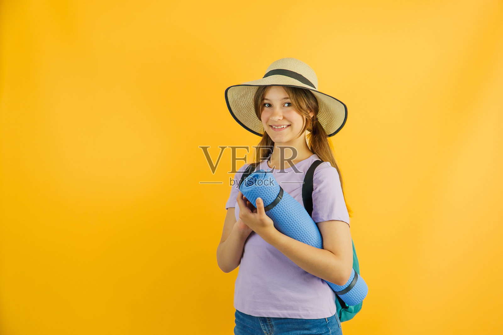 快乐可爱的小女孩旅行者背着徒步背包，徒步旅行，站在黄色的背景上，戴着时髦的帽子，脸上带着快乐的表情，爱旅行照片摄影图片