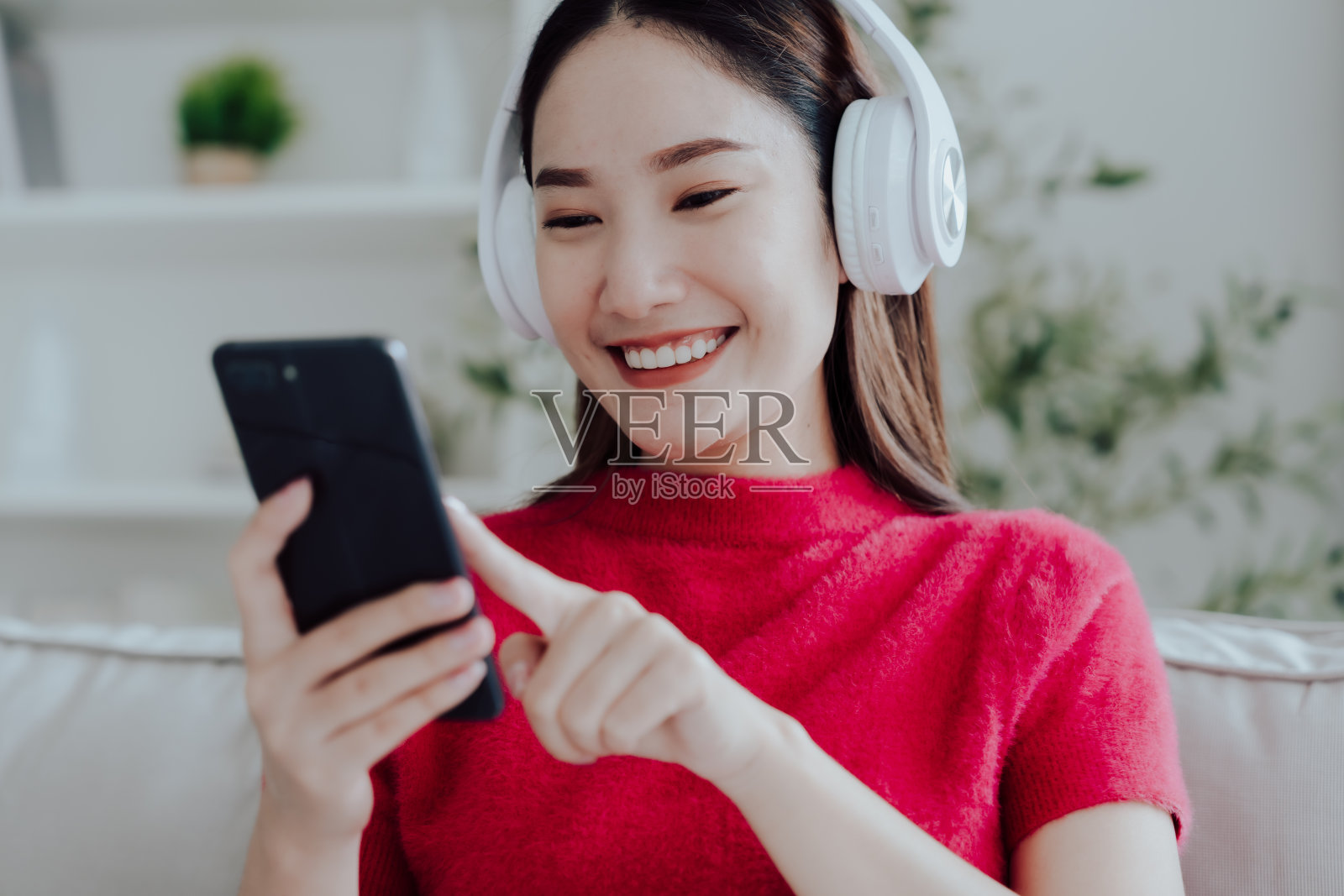 年轻的亚洲女子在家里的沙发上放松，用耳机听音乐的手机。人们的生活方式理念照片摄影图片