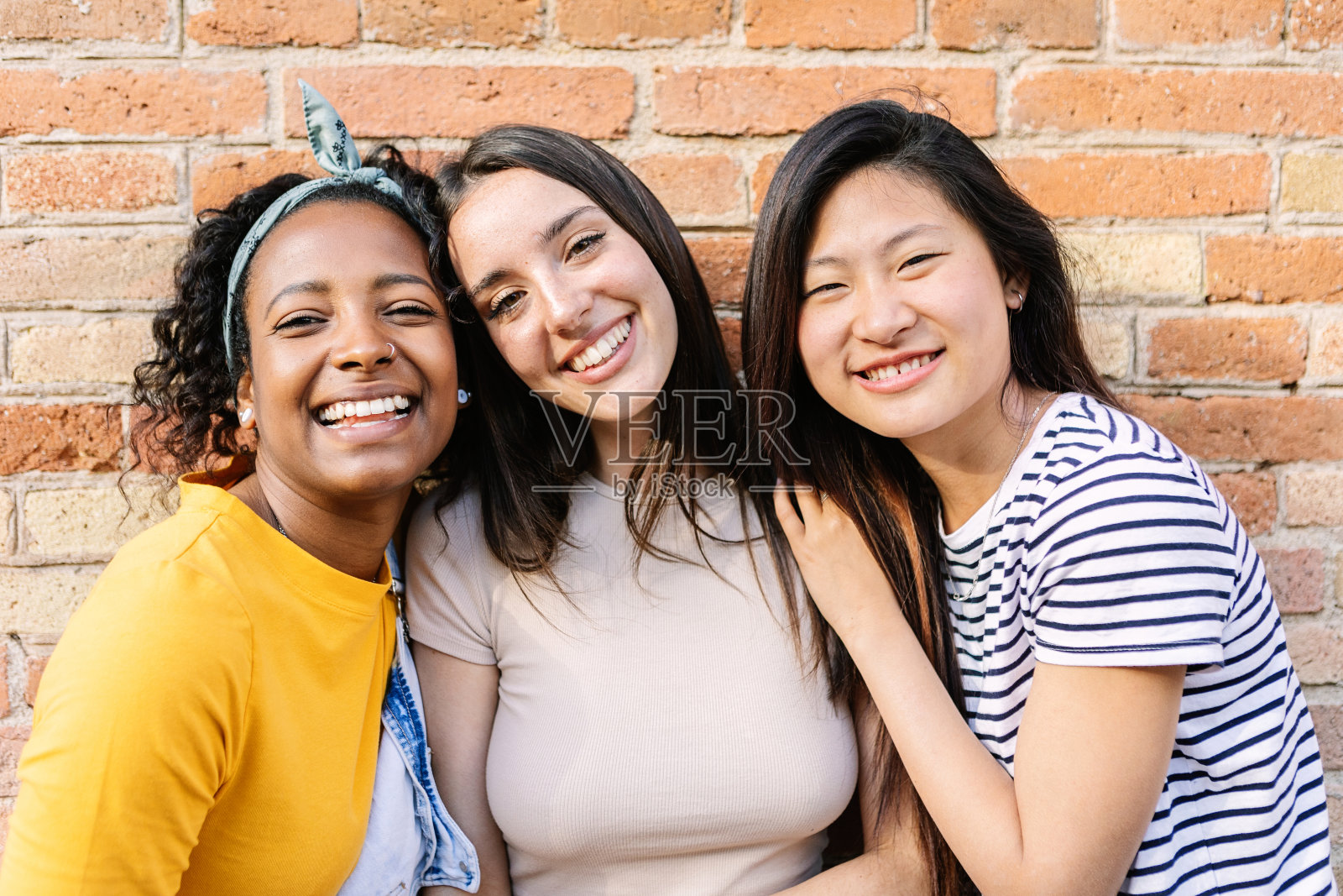 三位不同的年轻女性在户外对着相机微笑的肖像。照片摄影图片