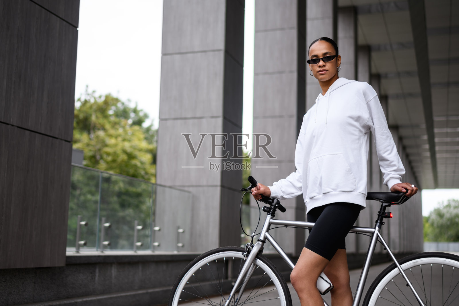 戴着时髦太阳镜的年轻非裔美国妇女站在街上的自行车旁照片摄影图片