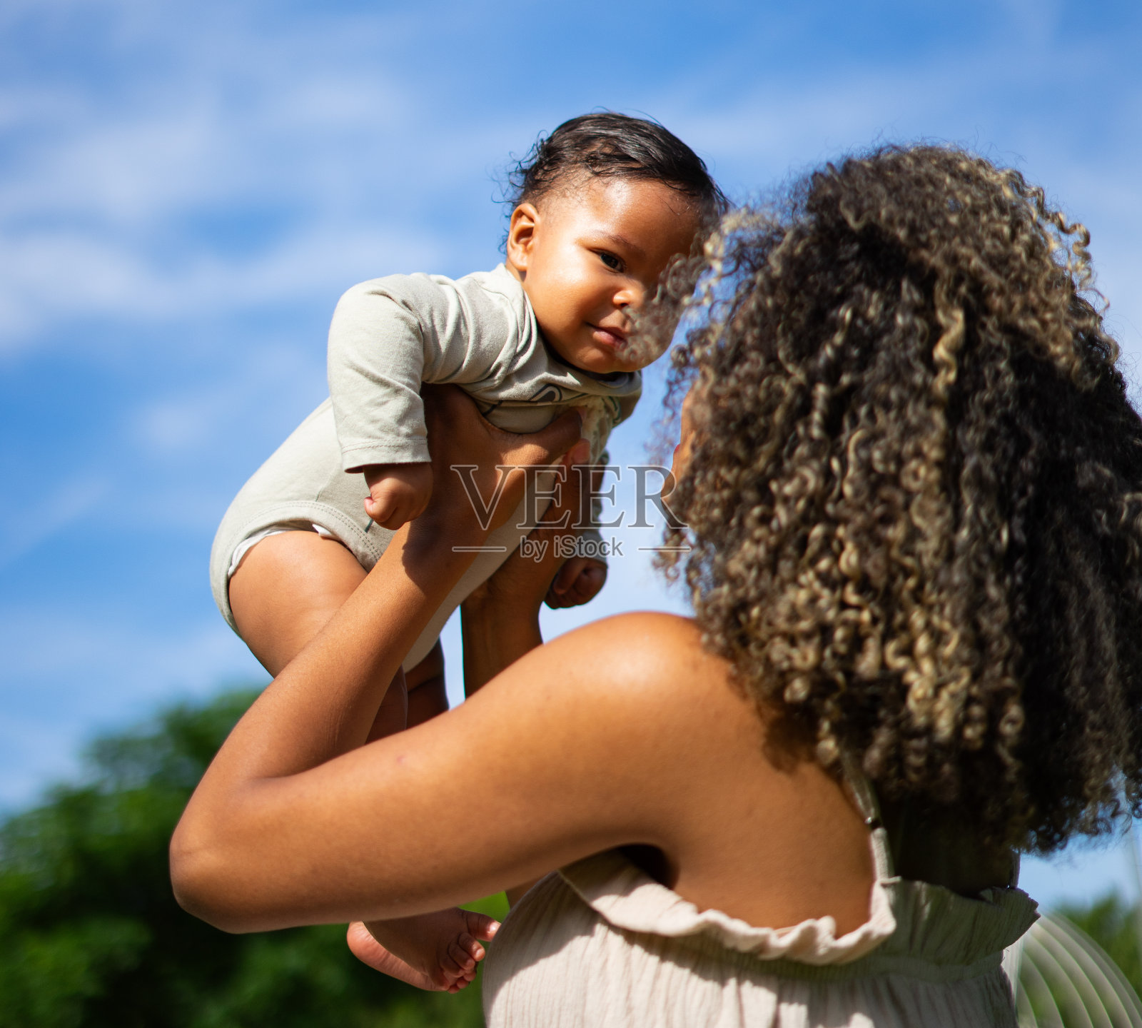 拉丁母亲与非洲头发抱着她的婴儿与蓝天背景照片摄影图片