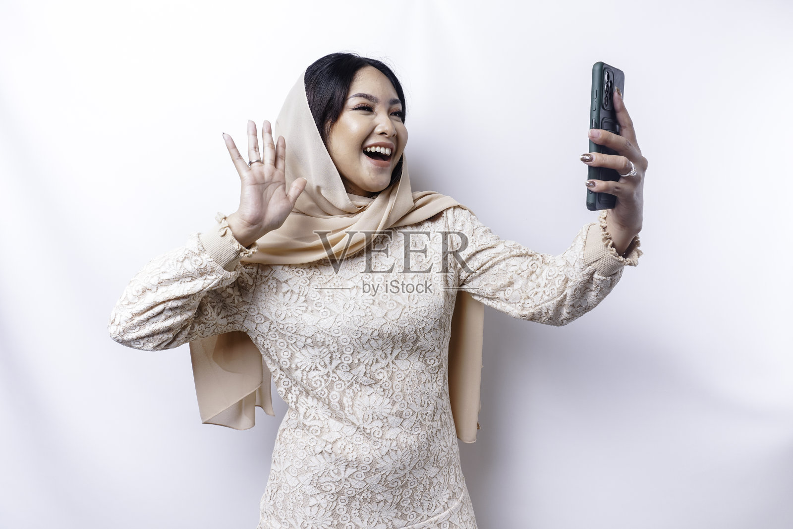 一个戴着头巾的快乐的亚洲穆斯林妇女的肖像，拿着她的手机，被白色的背景隔开照片摄影图片