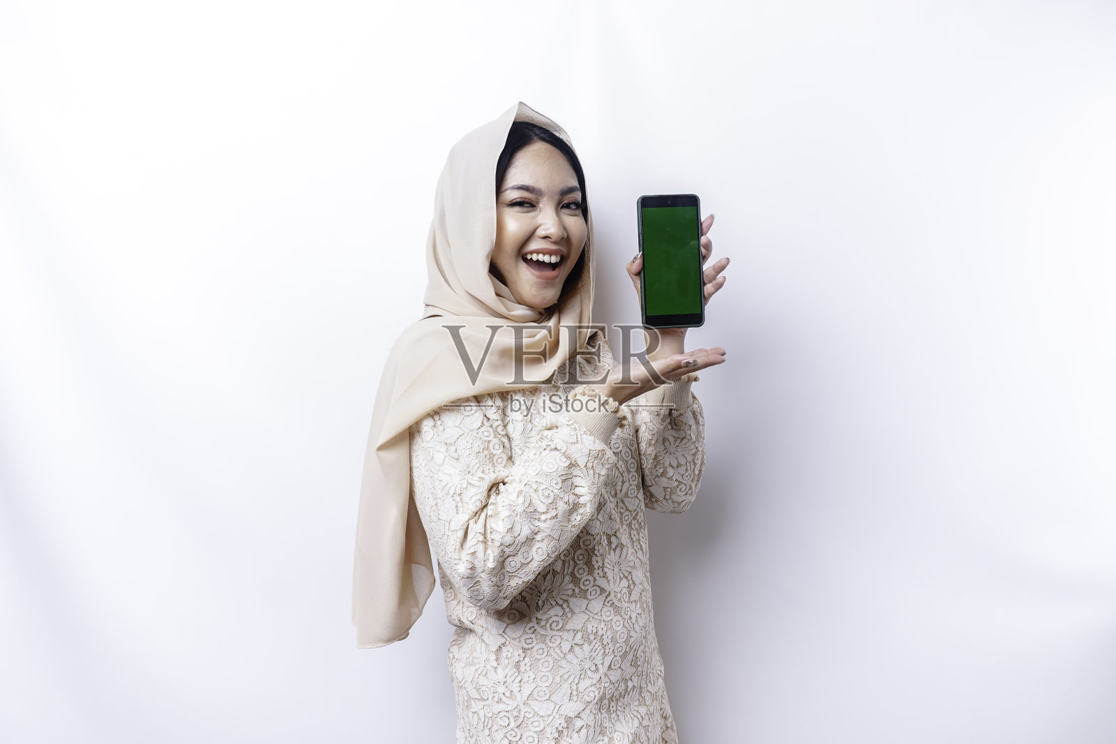一个戴着头巾的快乐的亚洲穆斯林妇女的肖像，展示着她的手机屏幕，被白色的背景隔开照片摄影图片