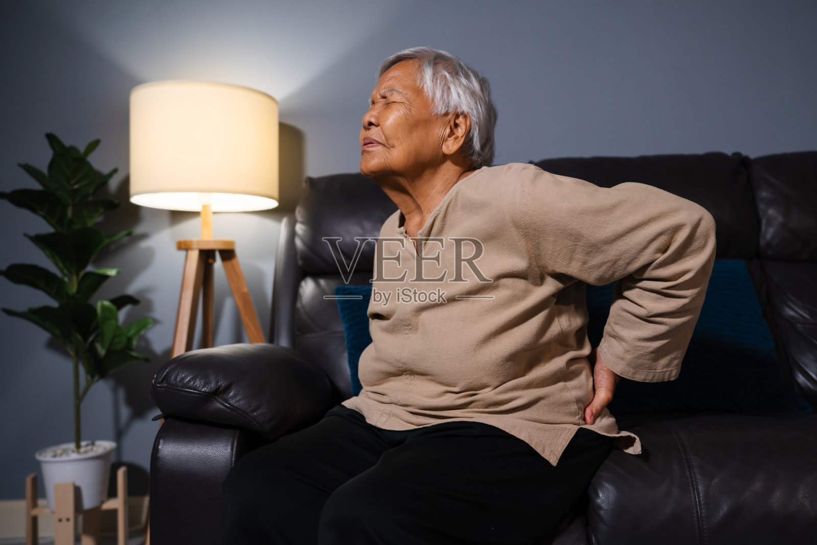 老妇人晚上坐在客厅的沙发上背痛照片摄影图片