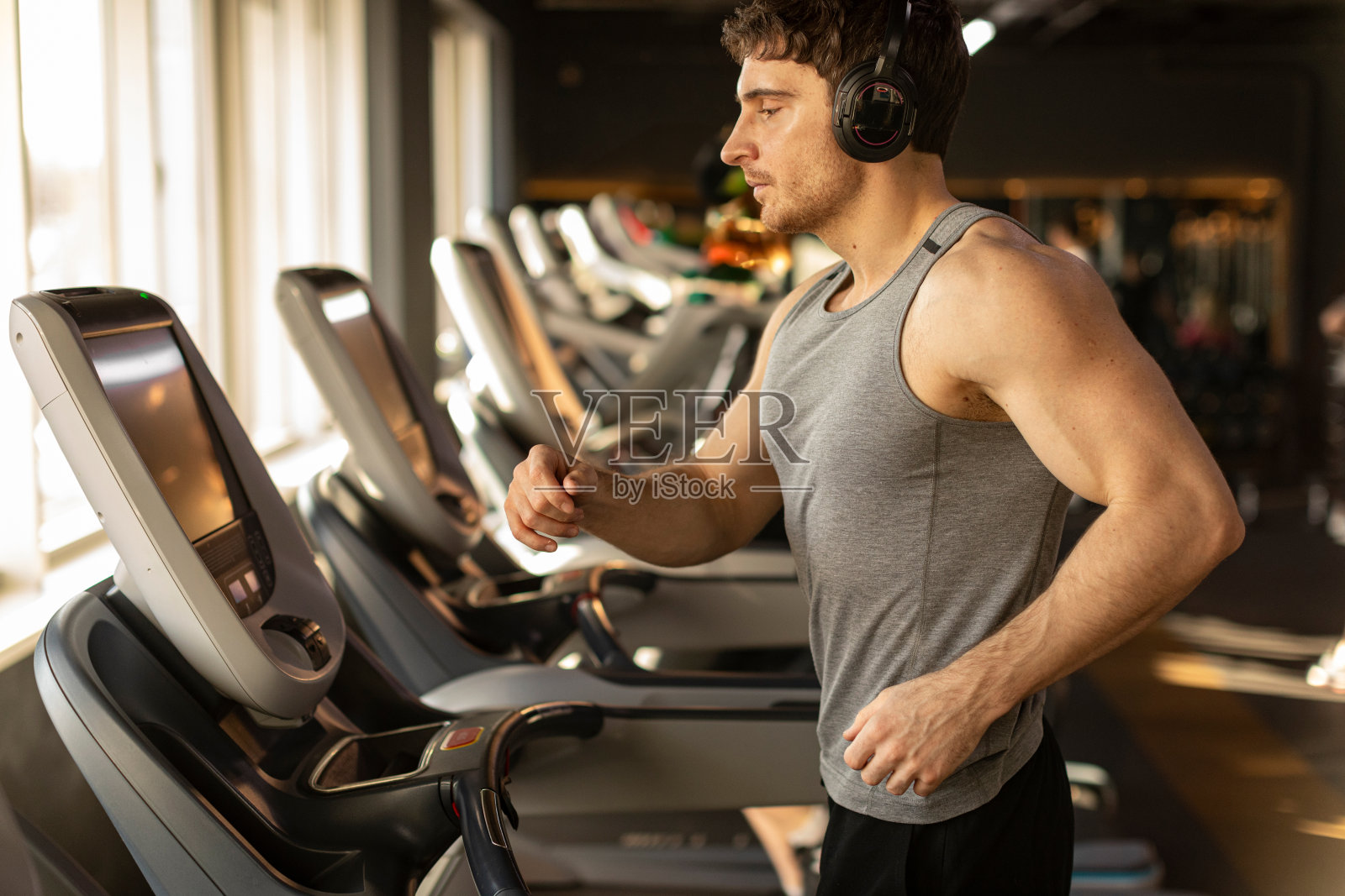 专注的帅哥在跑步机上跑步，戴着耳机听音乐。健康运动生活理念。照片摄影图片