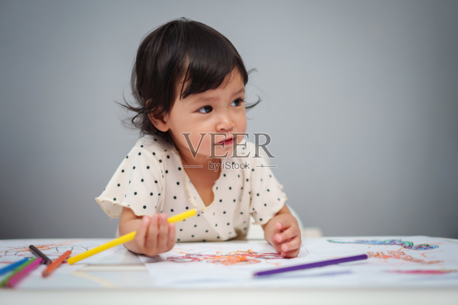 蹒跚学步的婴儿在桌子上玩和训练用彩色铅笔画画照片摄影图片