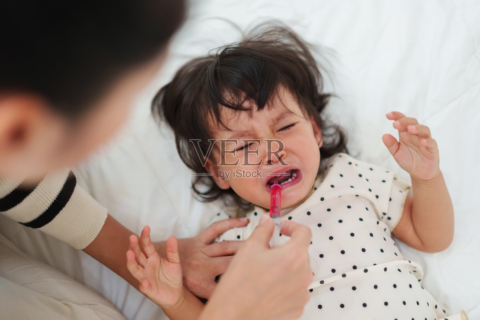 母亲用注射器给女婴喂药液。生病的哭闹小孩照片摄影图片