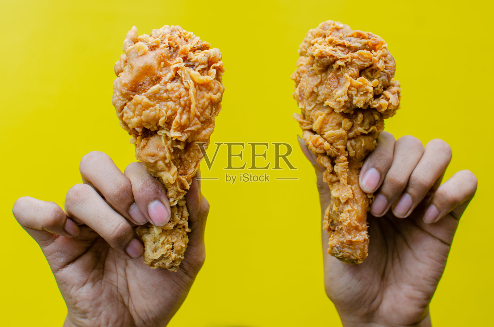 拿着炸鸡的手紧紧地隔在黄色的背景上照片摄影图片