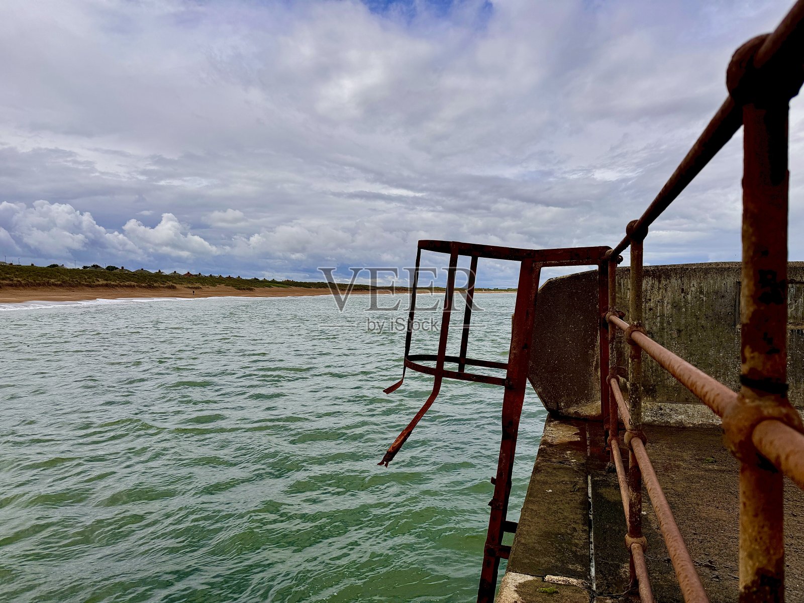 诺森伯兰郡地平线上的沙丘映衬着生锈的金属栏杆和海水照片摄影图片