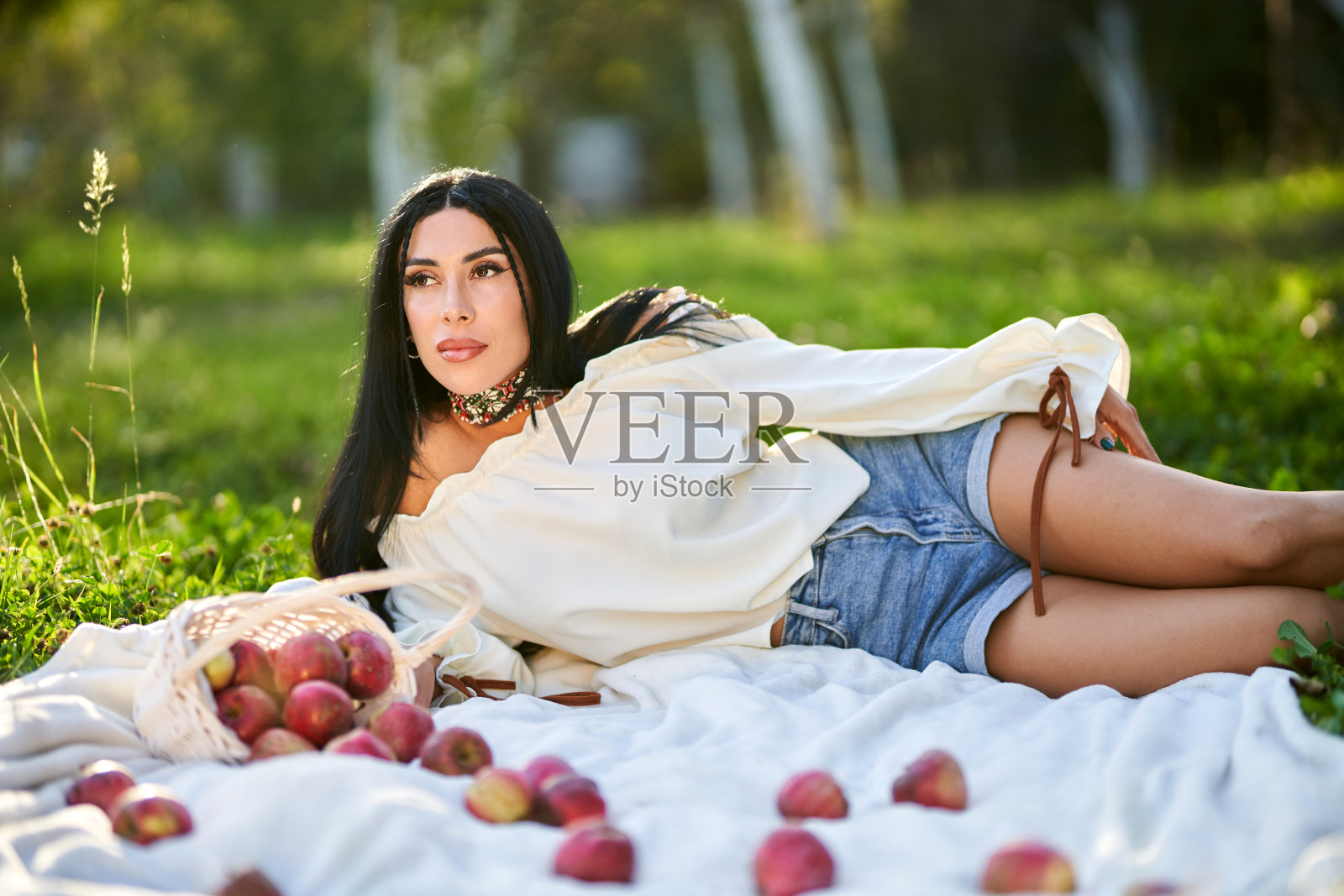 美丽的女人躺在果园草地上的地毯上。照片摄影图片
