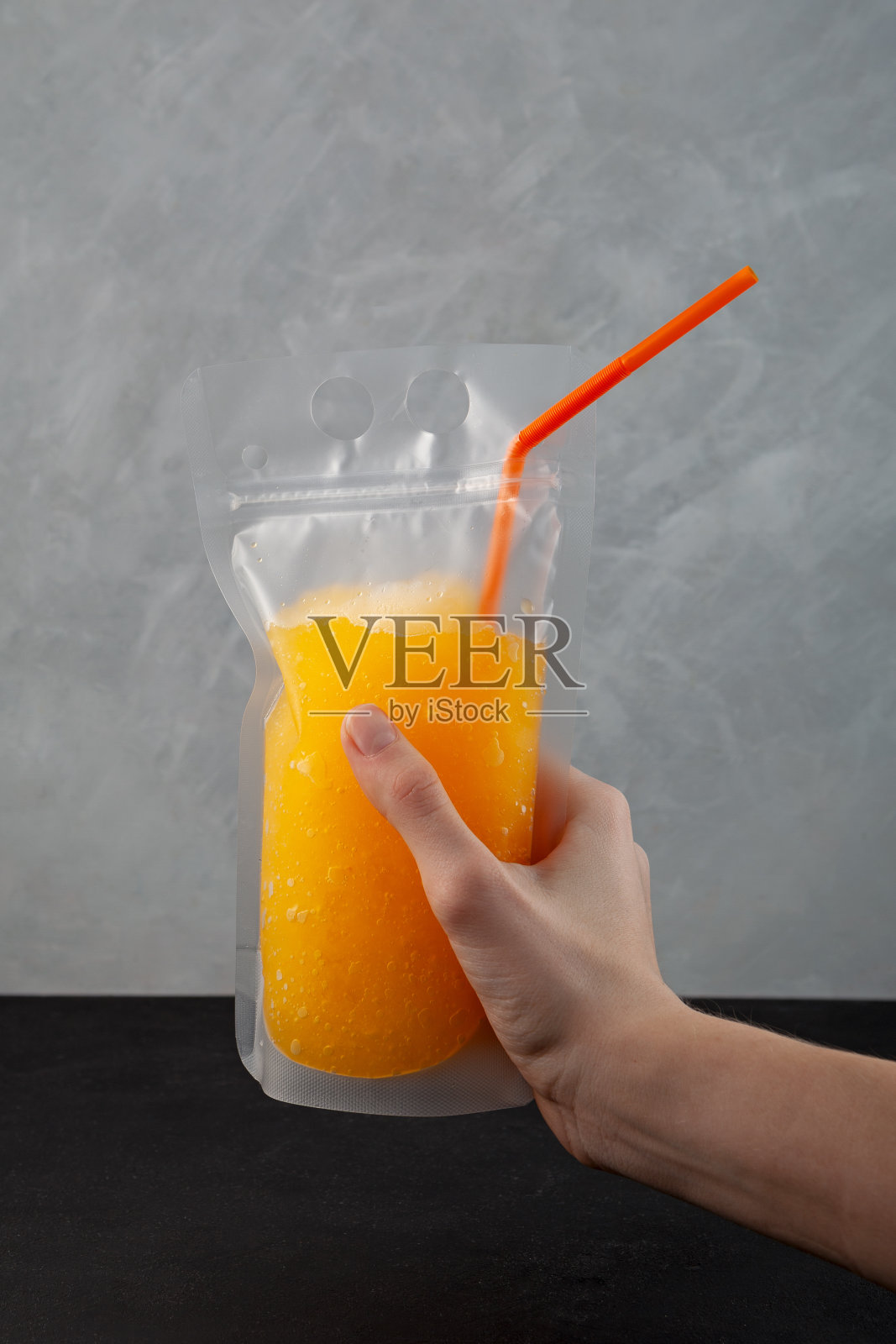 成人柑橘饮料可重复使用的袋与吸管在妇女手中。橙酒泥。酒精鸡尾酒装在防溅塑料袋里。清爽夏日带走饮品照片摄影图片