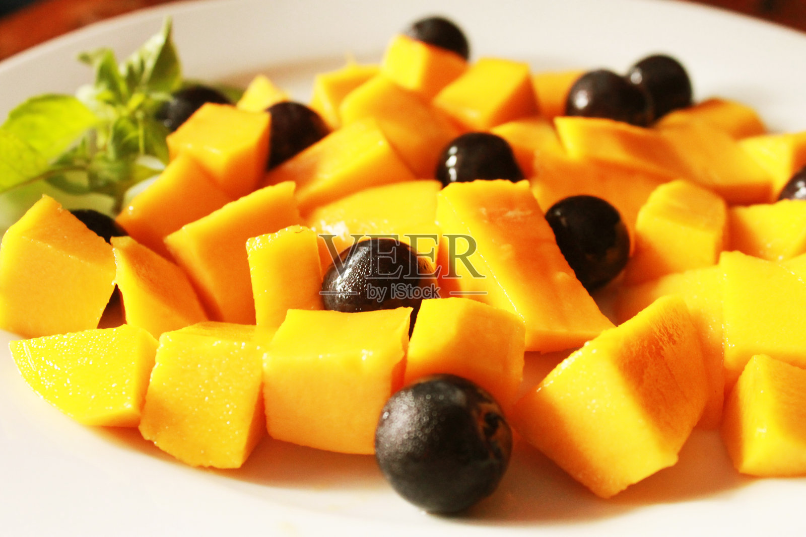 特写:美味的水果沙拉，新鲜的芒果和葡萄放在白色盘子里照片摄影图片