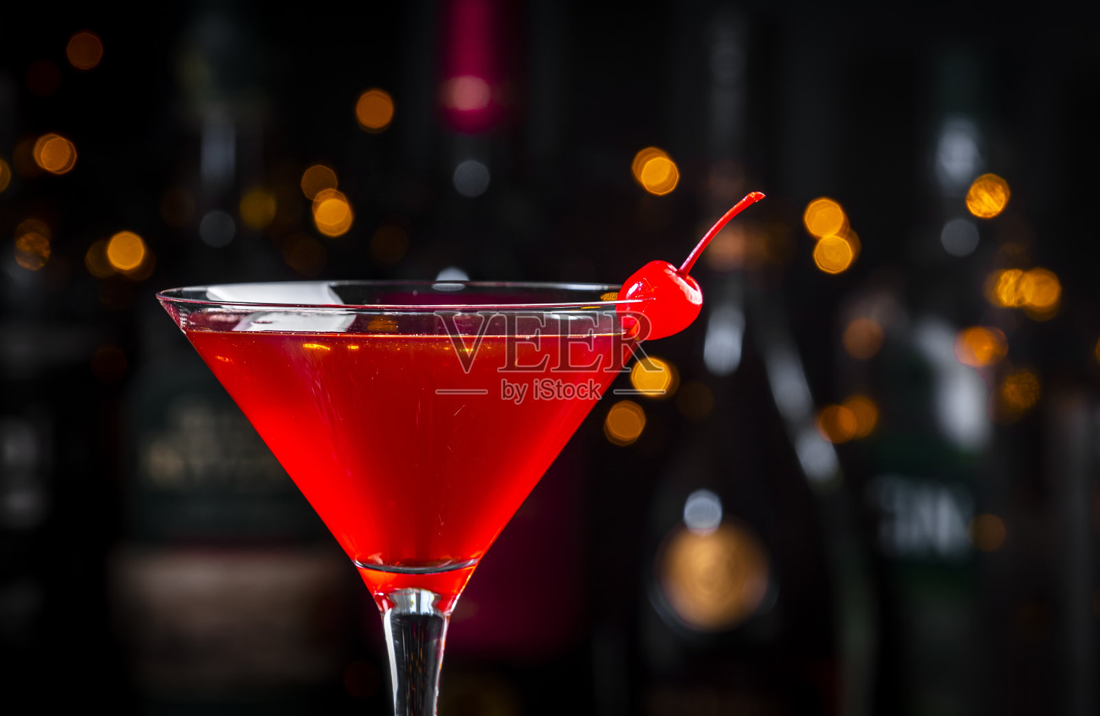 深色背景的樱桃红色酒精鸡尾酒，吧台上摆放着酒瓶，特写照片摄影图片