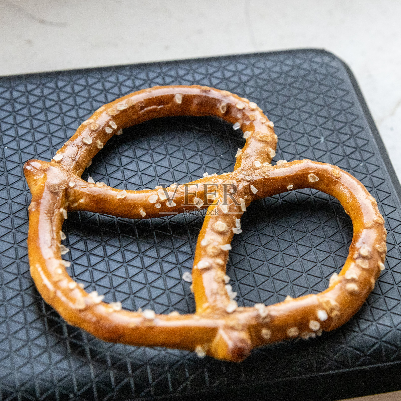 黑色托盘上的金棕色椒盐卷饼特写，聚焦面团纹理和闪亮的盐粒照片摄影图片