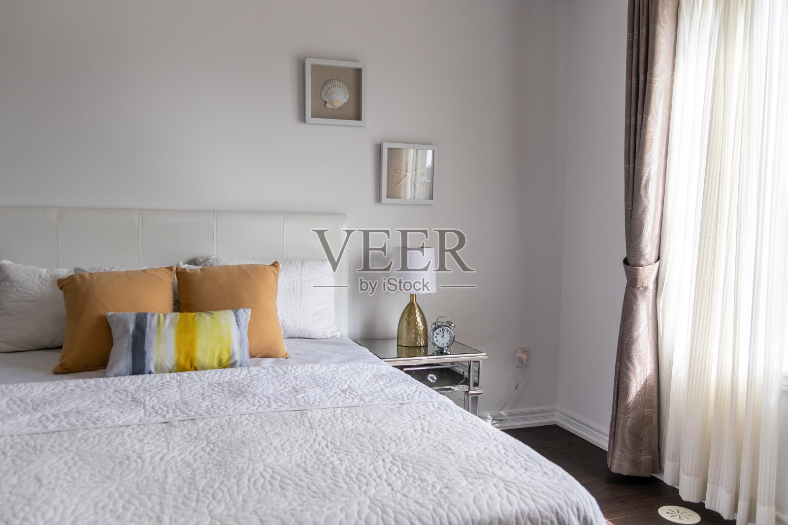 明亮的卧室，白色的床罩，棕色和黄色的枕头，镜子边桌照片摄影图片